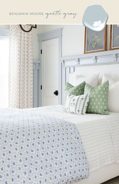 a white bed with blue and green pillows in a bedroom next to a window, framed pictures on the wall