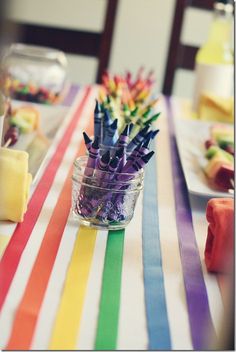 there are many colorful crayons in the glass on this table cloth, along with other food items