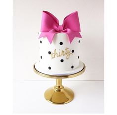 a white and black polka dot cake with pink bow on top that says, something chic