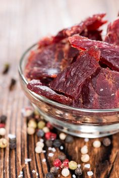 a glass bowl filled with red meat sitting on top of a wooden table next to pepper flakes