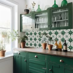 a kitchen with green cabinets and plants in pots on the counter top, next to a window