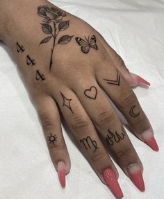 a woman's hand with tattoos on it and two fingers that have hearts, arrows, flowers, and butterflies