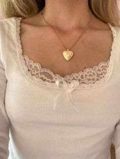 a woman wearing a necklace with a heart shaped pendant on the front of her neck