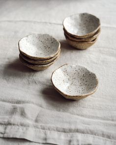 four speckled bowls sitting on top of a white cloth