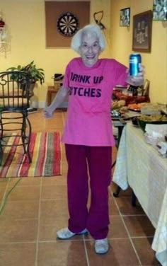 an older woman in pink shirt and purple pants standing next to table with food on it