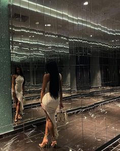 a woman standing in front of a mirror holding a handbag and looking at her reflection