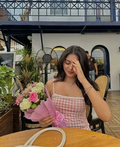 a woman sitting at a table with flowers in front of her and covering her eyes