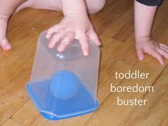 a toddler is playing with a blue ball in a plastic container on the floor