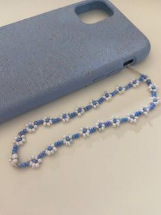 a cell phone case with a blue and white beaded necklace next to it on a table