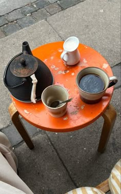 two cups of coffee sit on an orange table next to a person's feet