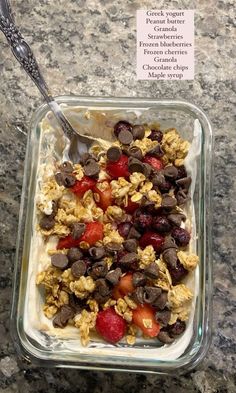 a glass dish filled with cereal and fruit on top of a counter next to a spoon