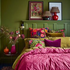 a bedroom with green walls, pink and yellow bedding and pictures on the wall