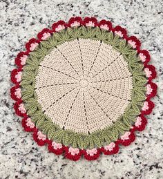 a crocheted doily with red, green and white flowers on it sitting on a granite surface