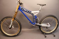 a blue and white mountain bike with gold rims on the front wheel, standing against a gray background