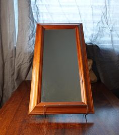 a mirror sitting on top of a wooden table next to a stuffed animal and curtain