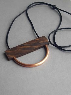 Minimalist wood + copper semircle necklace. Handmade from a beautiful, rich and highly figured piece of walnut wood. Threaded onto a simple black satin (2mm) cord for a contemporary look. The wood has been sealed with organic beeswax to enhance the natural colour and grain. Looks great at a longer length but the charred wood slider bead means that it can be worn long or shorter. The wood is 6.5cm x 1.7cm, 4mm thick. Light in weight and easy on the eye. The copper has been sealed but may tarnish Wood And Brass Necklace, Adjustable Brown Artistic Necklace, Artisan Natural Wood Necklaces, Unique Brown Resin Necklaces, Nature-inspired Brown Wooden Jewelry, Wooden Jewelery, Simple Jewellery, Wood Jewelery, Charred Wood