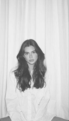 a black and white photo of a woman sitting in front of a curtain with long hair