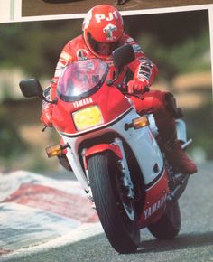 a man riding on the back of a red motorcycle down a street next to a sign