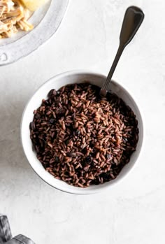 a white bowl filled with brown rice next to a spoon