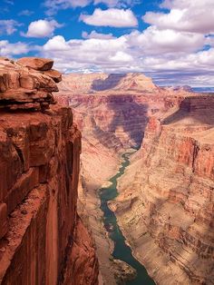 a man standing on the edge of a cliff overlooking a river and canyon in the distance