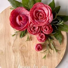 flowers are arranged on top of a cutting board with greenery and pink roses in the center