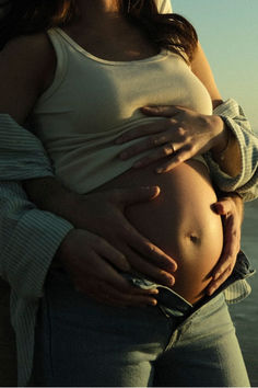 a pregnant woman is holding her belly in front of the ocean