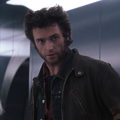 a man standing in front of a blue wall wearing a leather jacket and looking at the camera