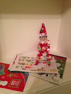 an elf is sitting on top of some christmas cards and other items in a box