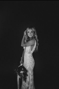 black and white photo of woman in wedding dress holding bouquet with hand on head, standing against dark background