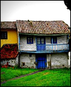 an old house with a blue door and red tile roof in the grass next to a yellow building