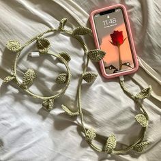 a cell phone laying on top of a bed next to a cord with a flower