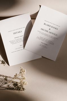 two folded wedding cards sitting on top of a table next to a vase with flowers