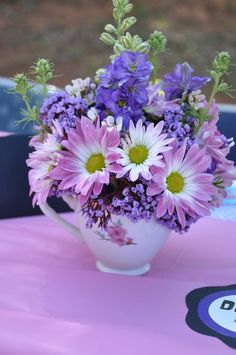 a vase filled with purple and white flowers sitting on top of a pink tablecloth