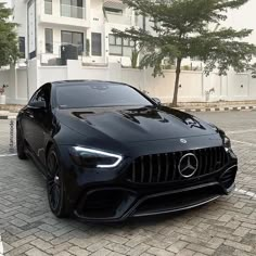 a black car parked in front of a building on a brick road next to trees