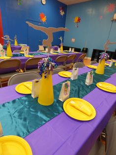 the table is set with yellow and purple plates, napkins, and vases