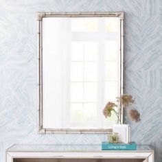 a mirror sitting on top of a dresser next to a vase with flowers in it