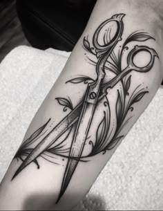 a black and white photo of a pair of scissors on someone's leg with tattoos