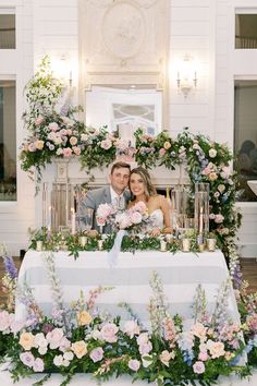 a bride and groom sitting at a table surrounded by flowers