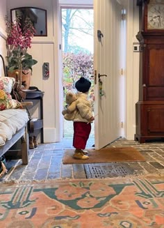 a little boy that is standing in front of a door with a teddy bear on the floor