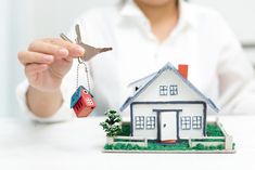 a woman holding keys to a model house and keychain in front of her