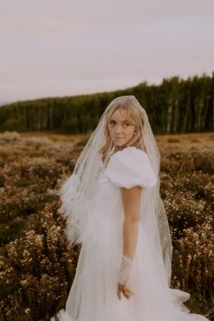 a woman in a white wedding dress and veil standing in a field with tall grass