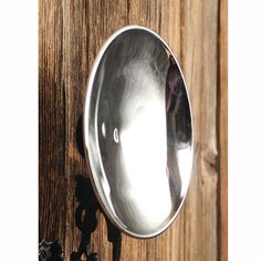 a round mirror mounted to the side of a wooden wall next to a hook on a door