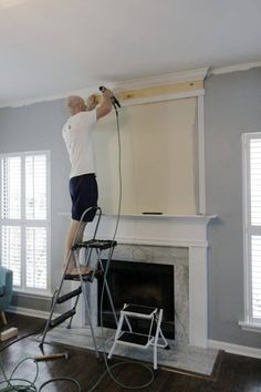 a man standing on a ladder painting a fireplace