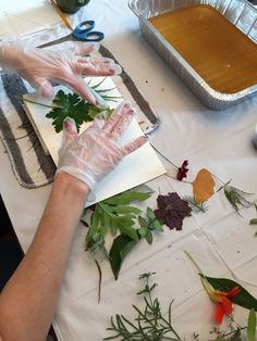 a person with gloves on cutting up leaves and flowers in front of a pan of food