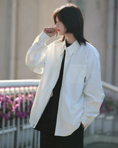 a woman in black pants and white jacket standing on a sidewalk with her hand to her face