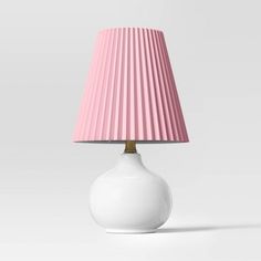 a white table lamp with a pink shade on the base and a gold colored light bulb