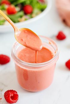 a spoon full of dressing with raspberries on the side and salad in the background