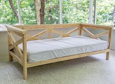 a wooden bed frame sitting on top of a floor next to a window with trees in the background