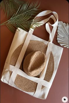 a straw hat sits on top of a white tote bag next to a palm leaf