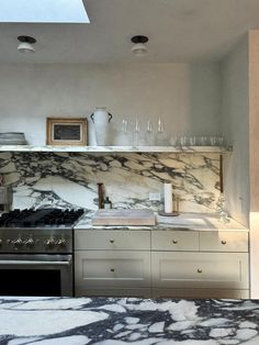 a kitchen with marble counter tops and stainless steel stove top oven, wine glasses on the shelves